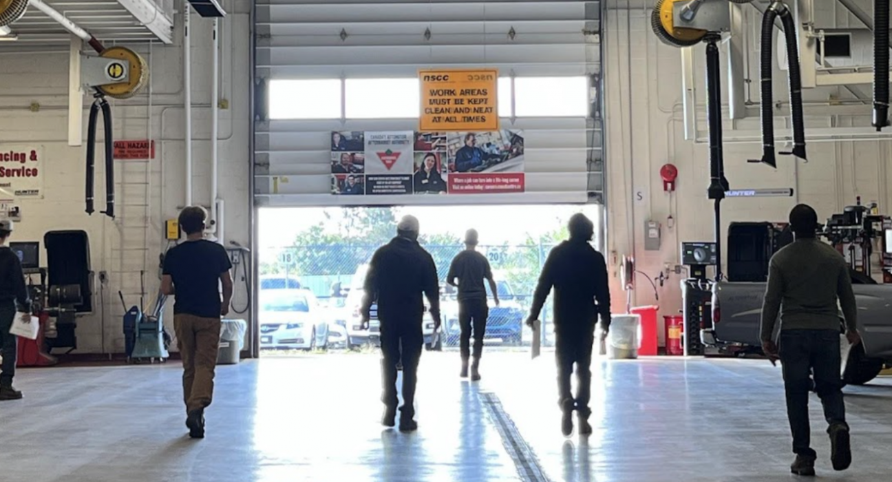 Cohort of 6 people in an automotive shop walking towards an open garage door