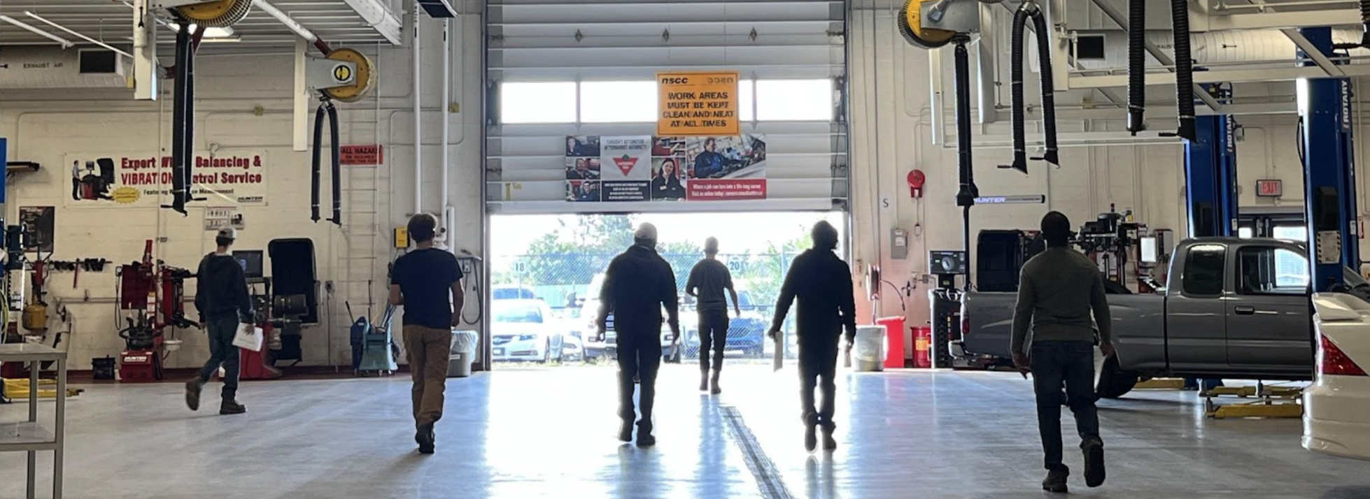 Cohort of 6 people in an automotive shop walking towards an open garage door